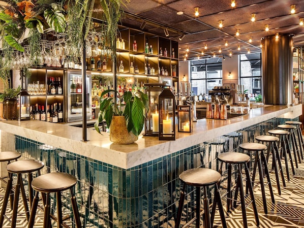 A bar area with a marble countertop, stools, and shelves stocked with bottles.
