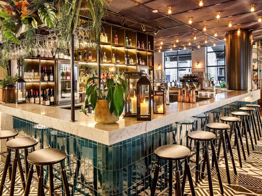 Un espace bar doté d’un comptoir en marbre, de tabourets et d’étagères remplies de bouteilles.