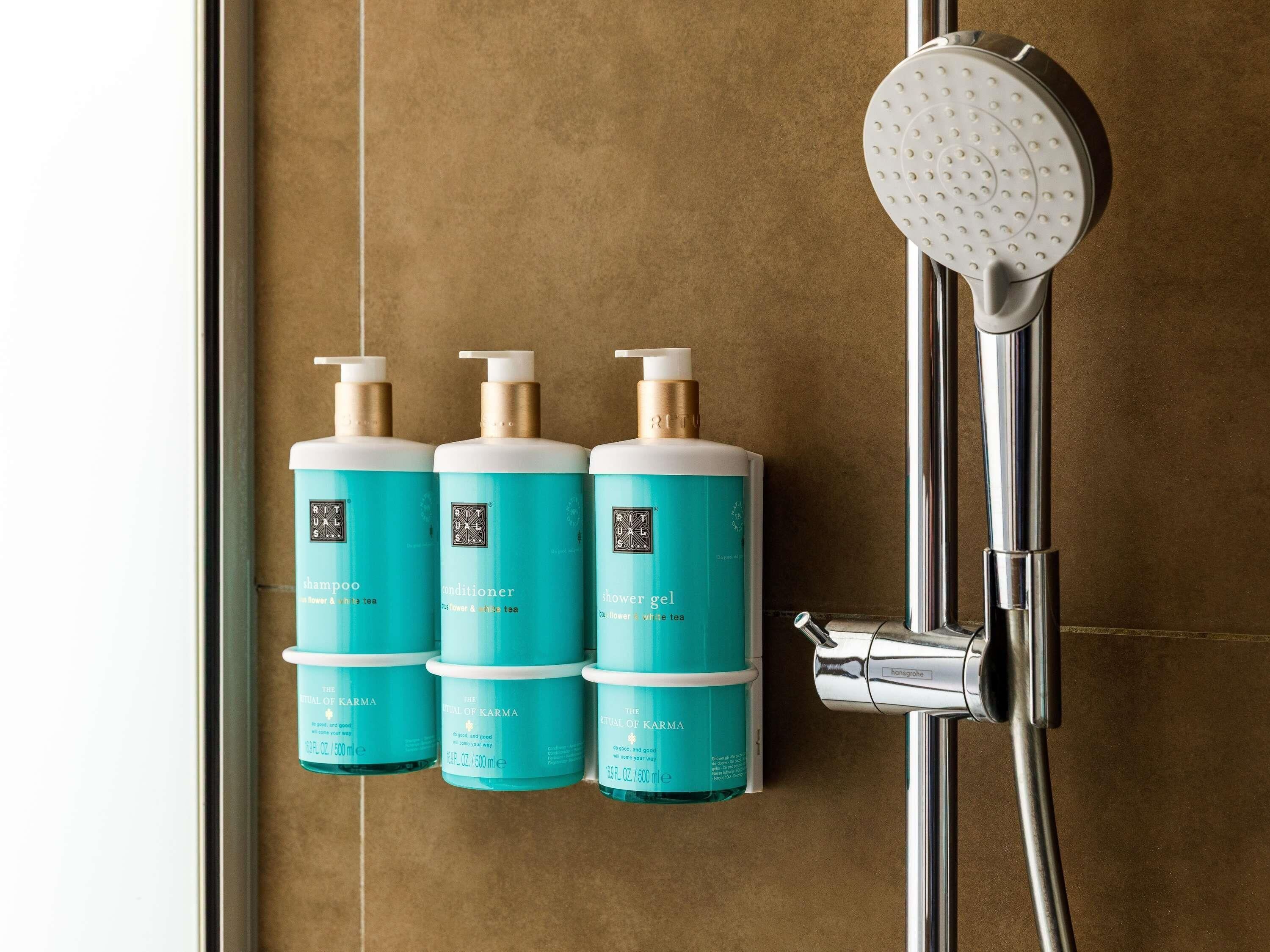 A bathroom with a shower, a towel rack, and three bottles of shampoo, conditioner, and shower gel.