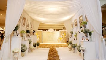 A wedding aisle with white drapes, a floral arrangement, and a photo display on either side.