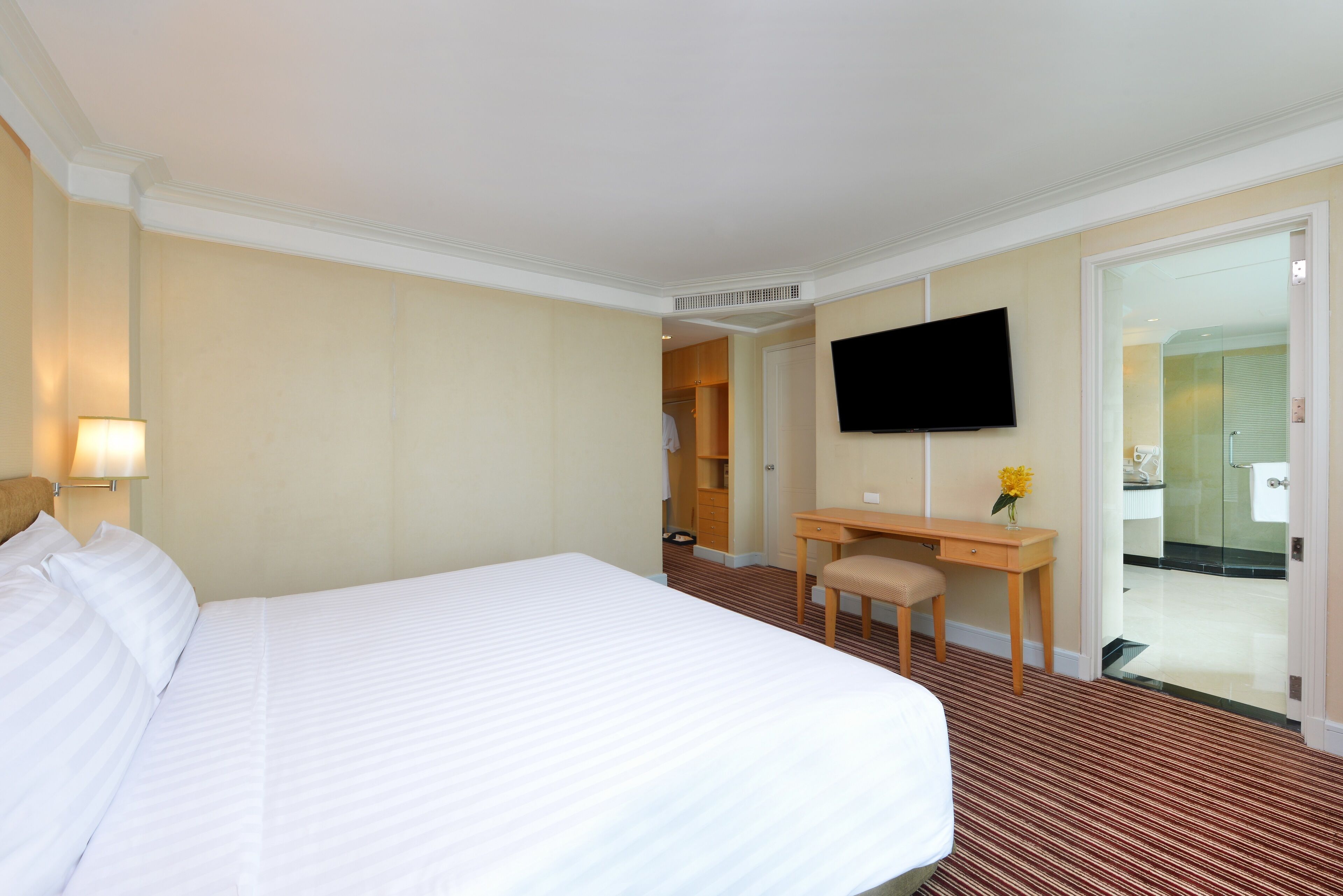 A hotel room with a large bed, a desk, a chair, a television, and a bathroom visible through an open door.