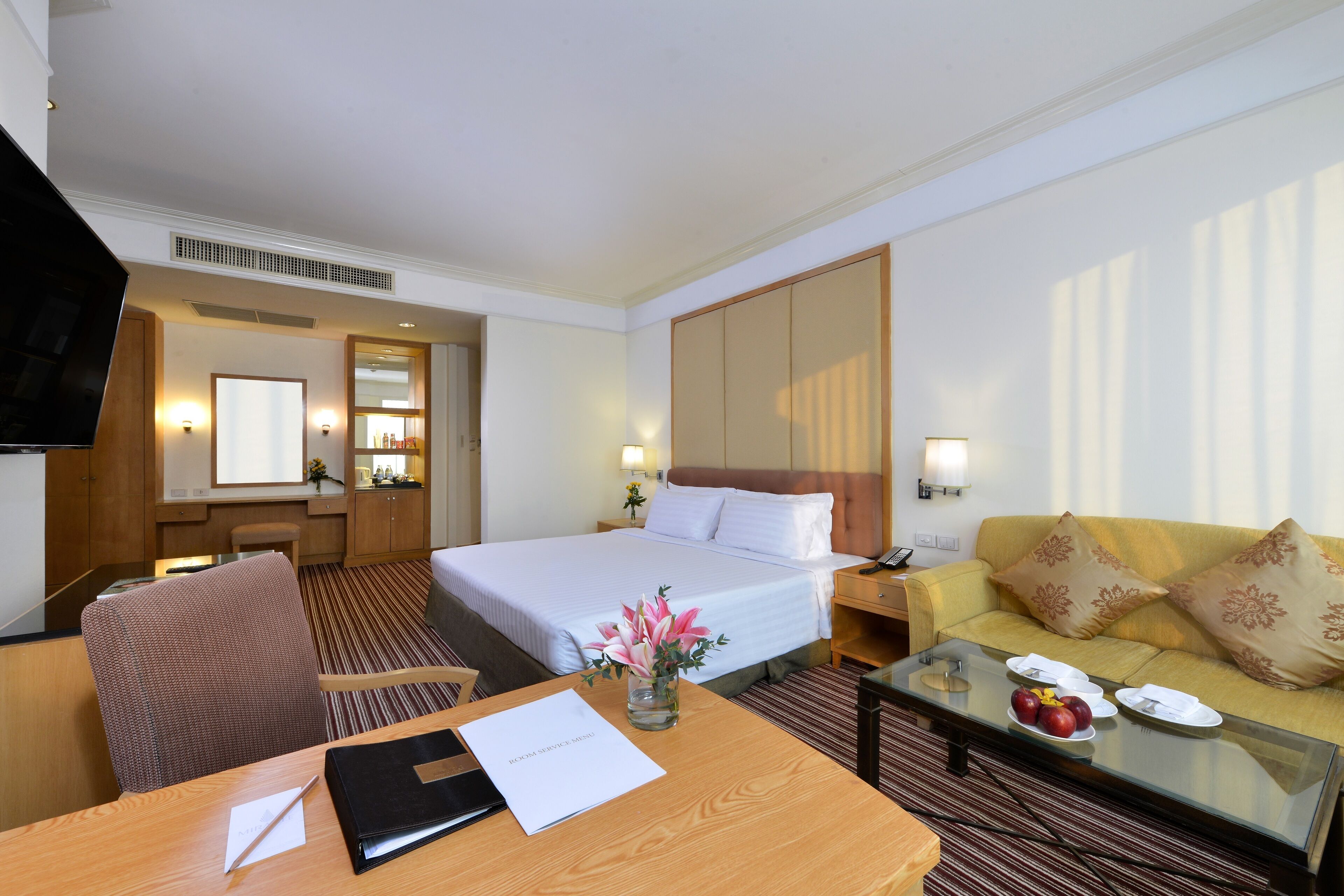 A hotel room with a bed, a sofa, a desk, and a TV.