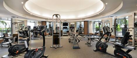 A modern gym with various exercise equipment, large windows, and a circular ceiling design.