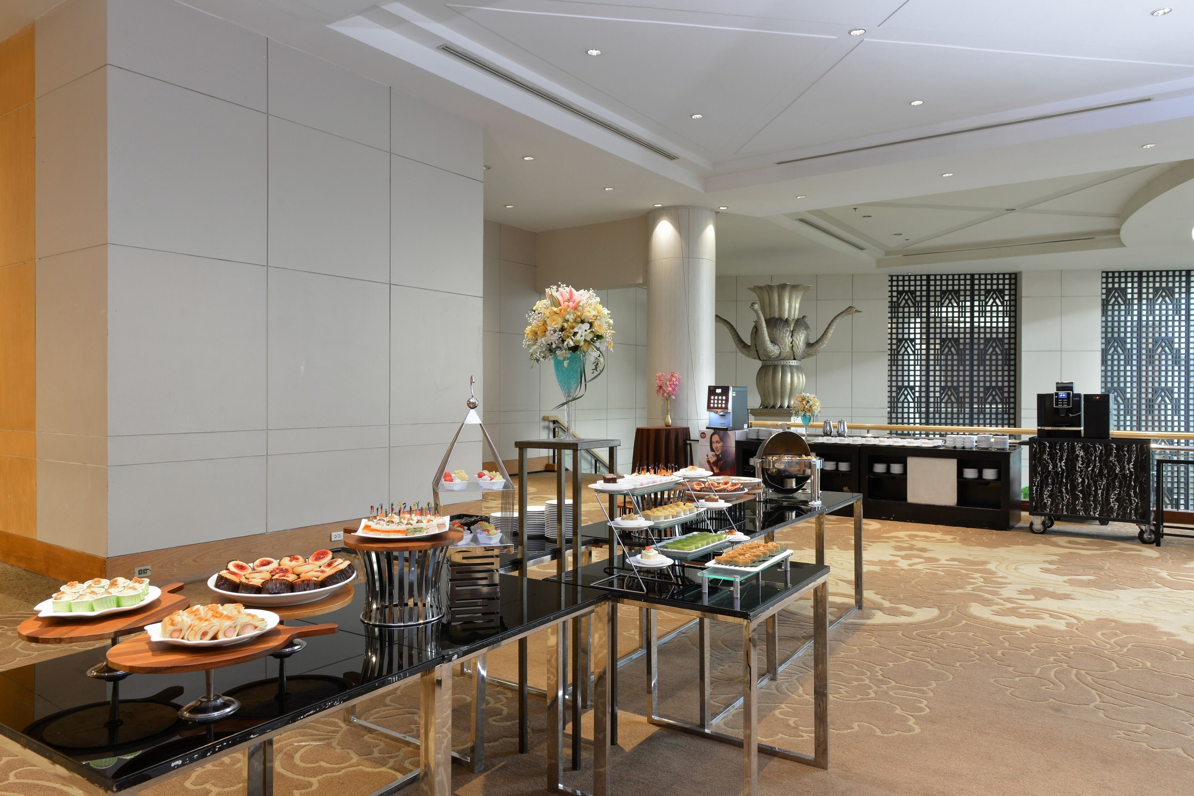 Un buffet avec différents plats présentés sur des plateaux, un vase décoratif et un espace salon agrémenté d’un tapis à motifs.
