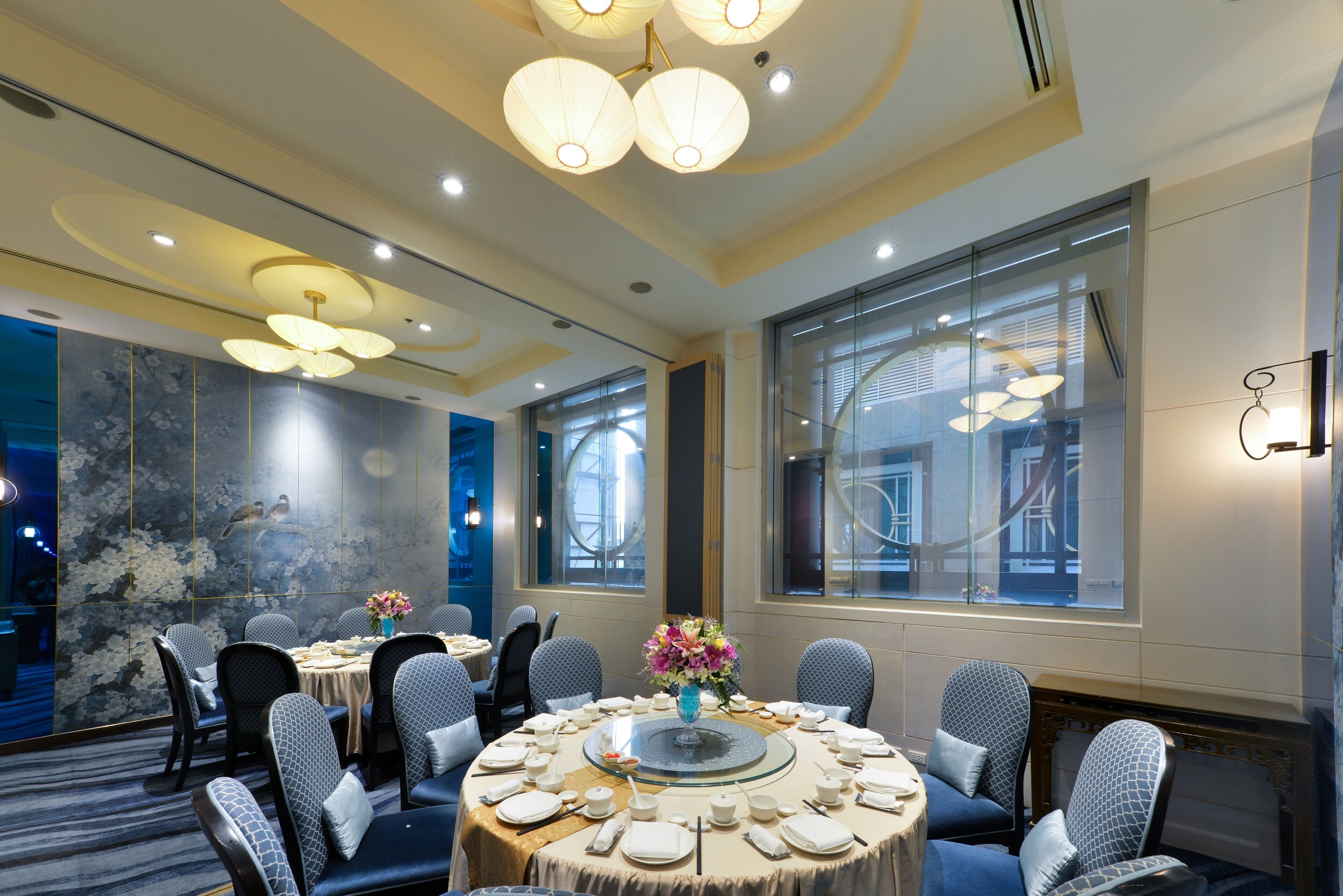 A conference room with round tables, chairs, and a large window with blinds.