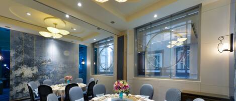 A conference room with round tables, chairs, and a large window with blinds.