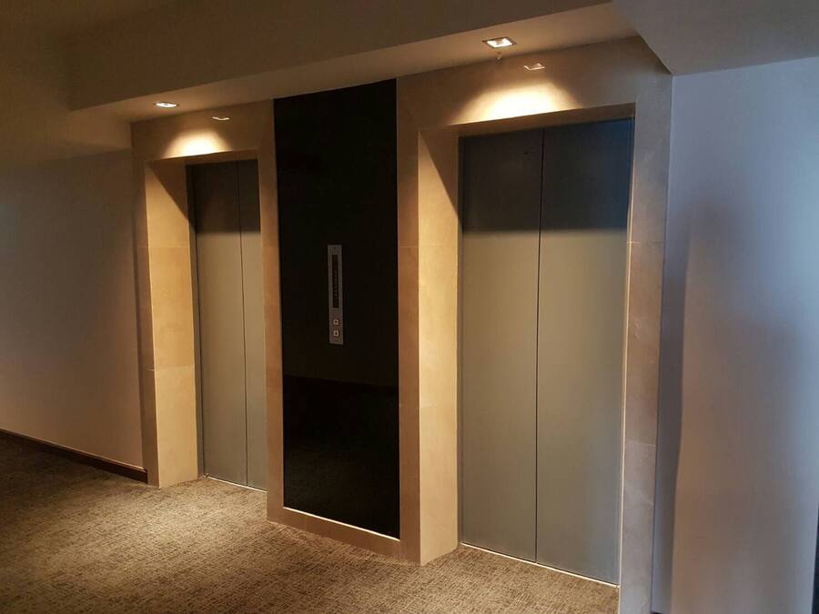 A hallway with three elevator doors, each with a control panel and illuminated by ceiling lights.