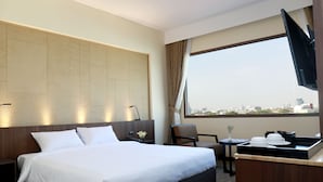 Hotelkamer met een groot bed, een bureau, een stoel, een televisie en een raam met uitzicht op de stad.