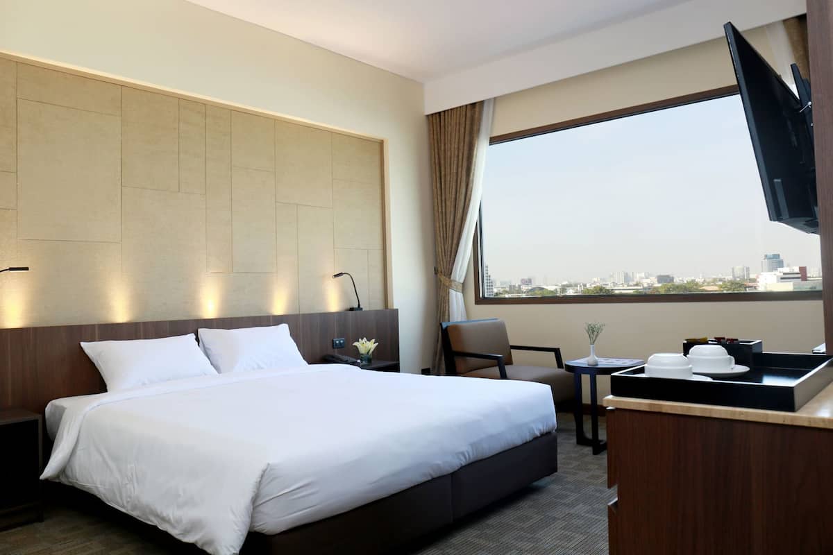 A hotel room with a bed, a desk, a chair, a TV, and a large window with a city view.