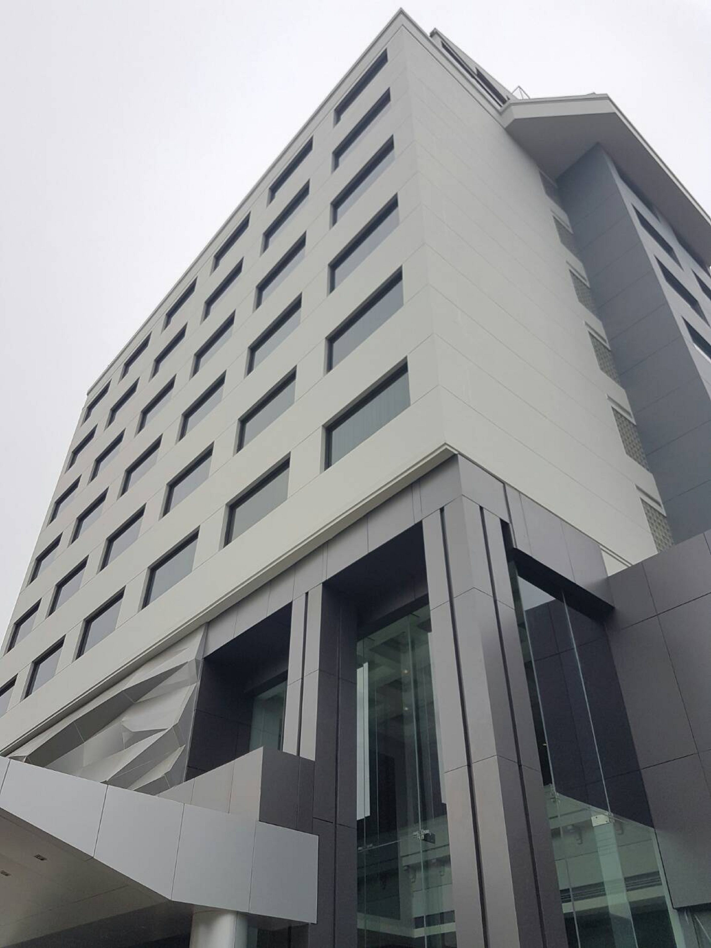 Ein modernes Gebäude mit einer geometrischen Fassade, zahlreichen Fenstern und einem markanten Glaseingang.