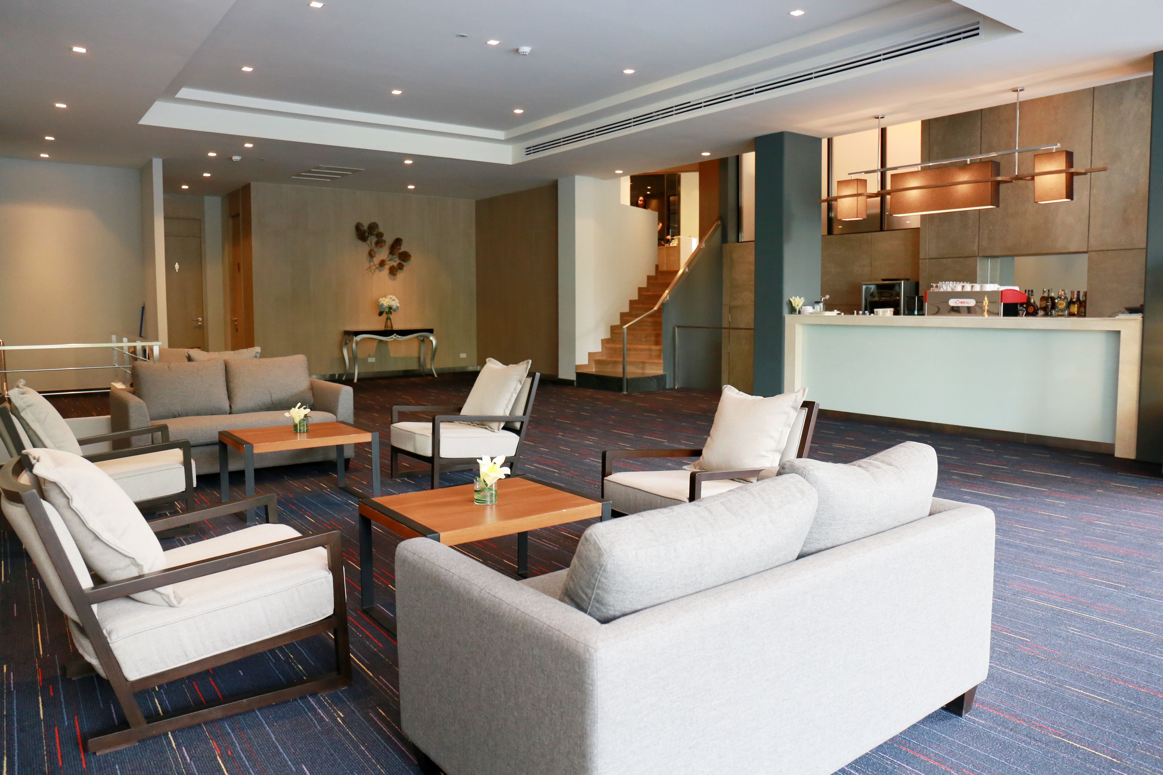 A modern hotel lobby with a seating area, a staircase, and a bar.