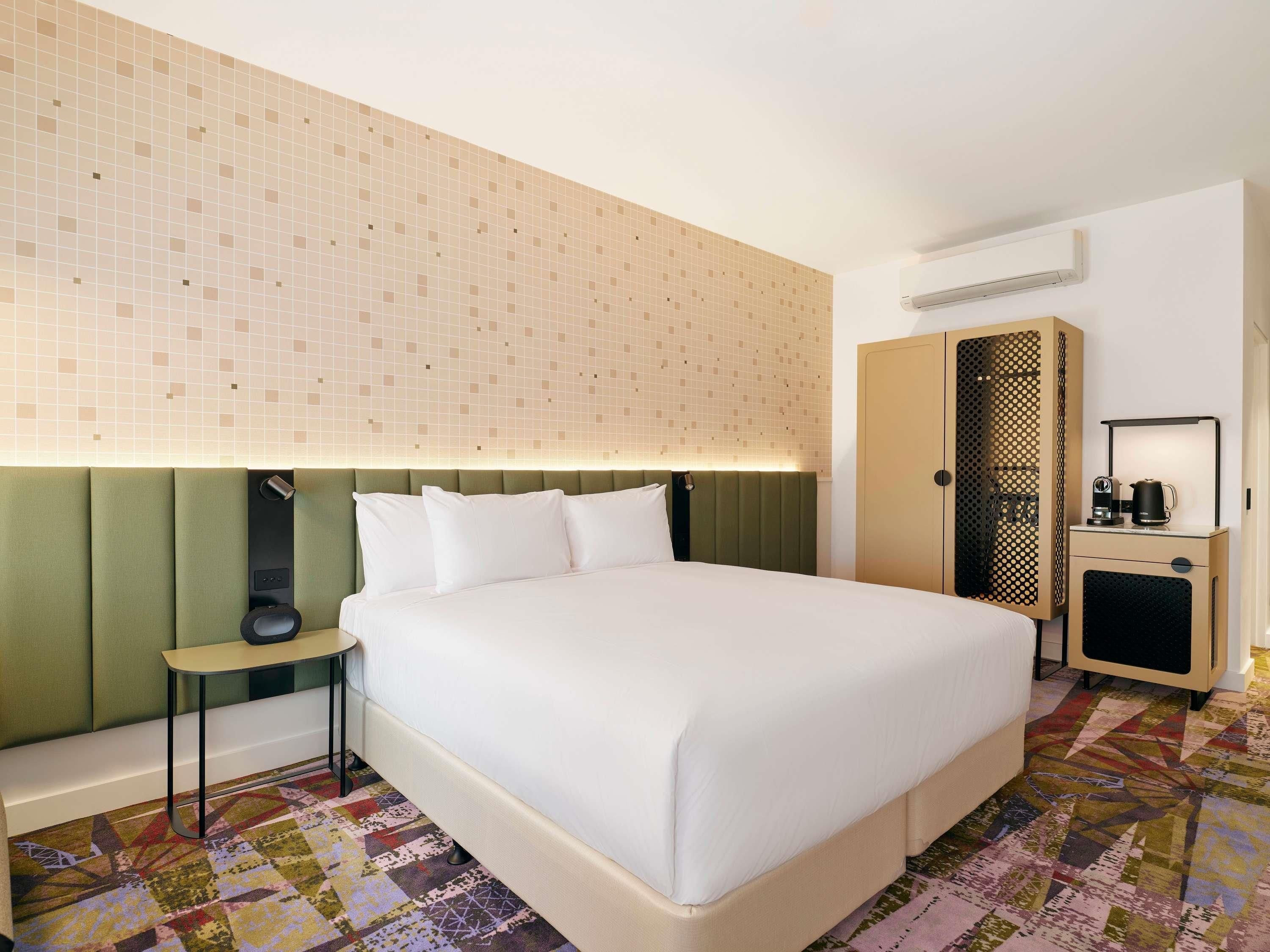 A hotel room with a large bed, a bedside table, a wardrobe, and a patterned carpet.