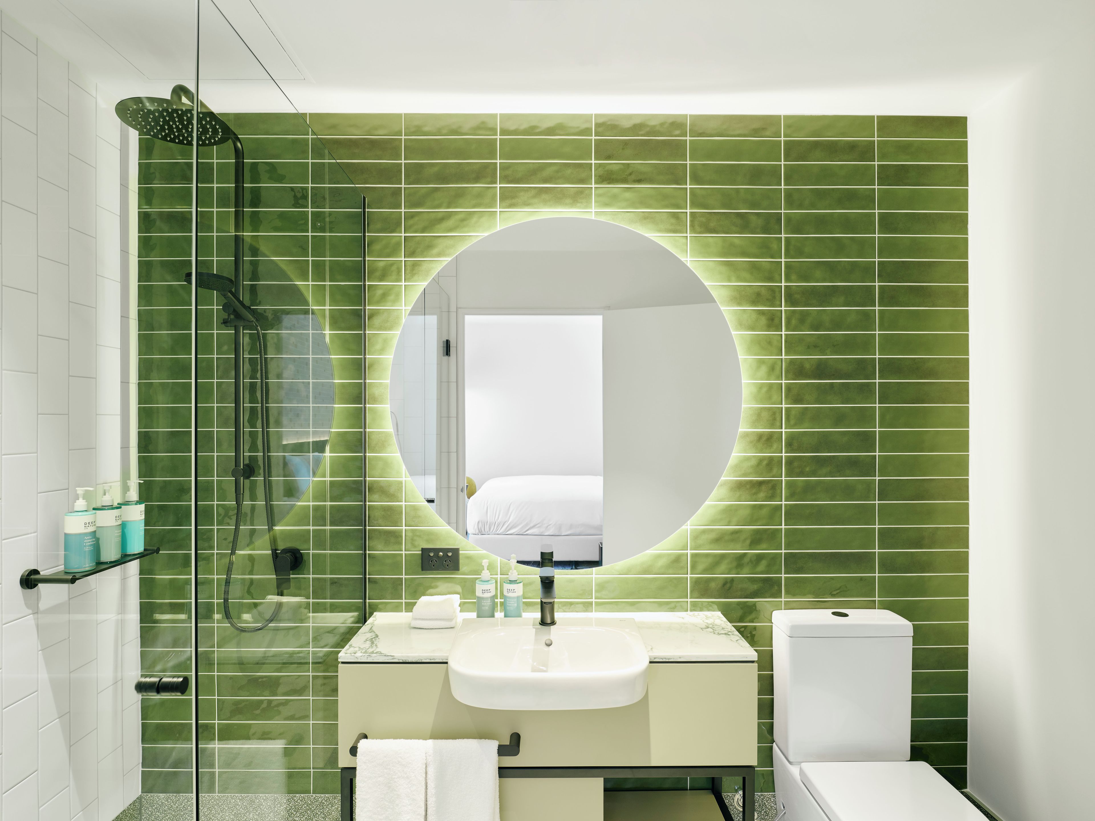 A bathroom with a green-tiled wall, a round mirror, a sink, and a toilet.