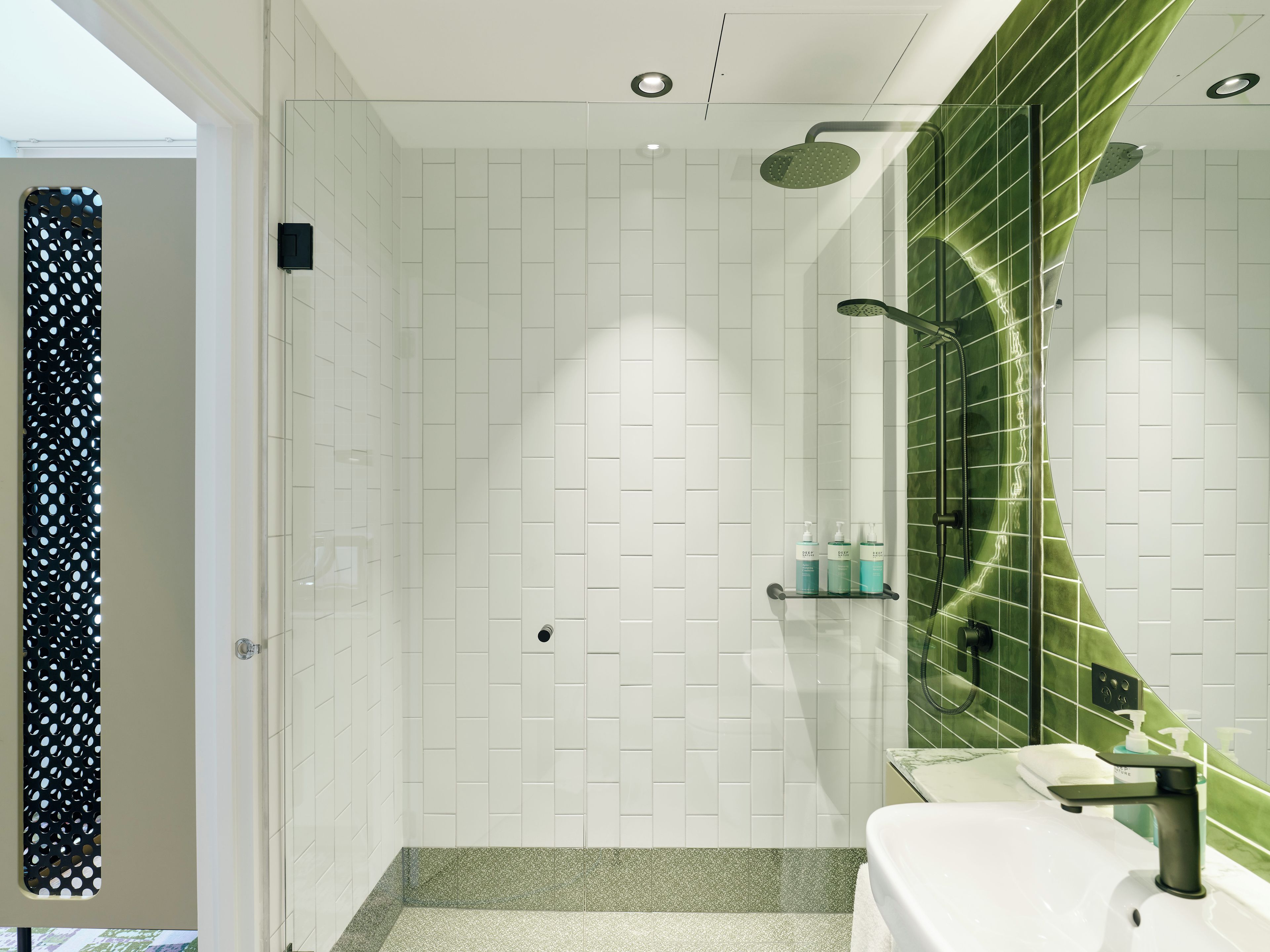 A modern bathroom with a shower, white tiled walls, a green accent wall, and a sink with a mirror.