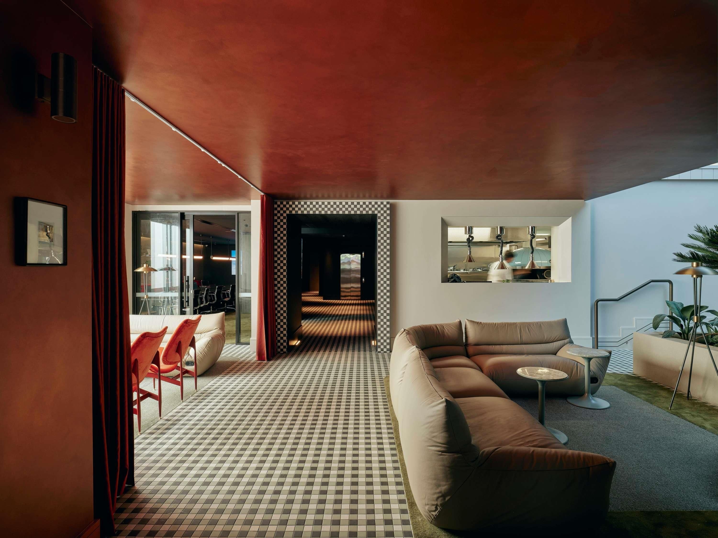 Una sala de estar moderna con piso a cuadros, un sofá marrón y una zona de comedor con sillas rojas.