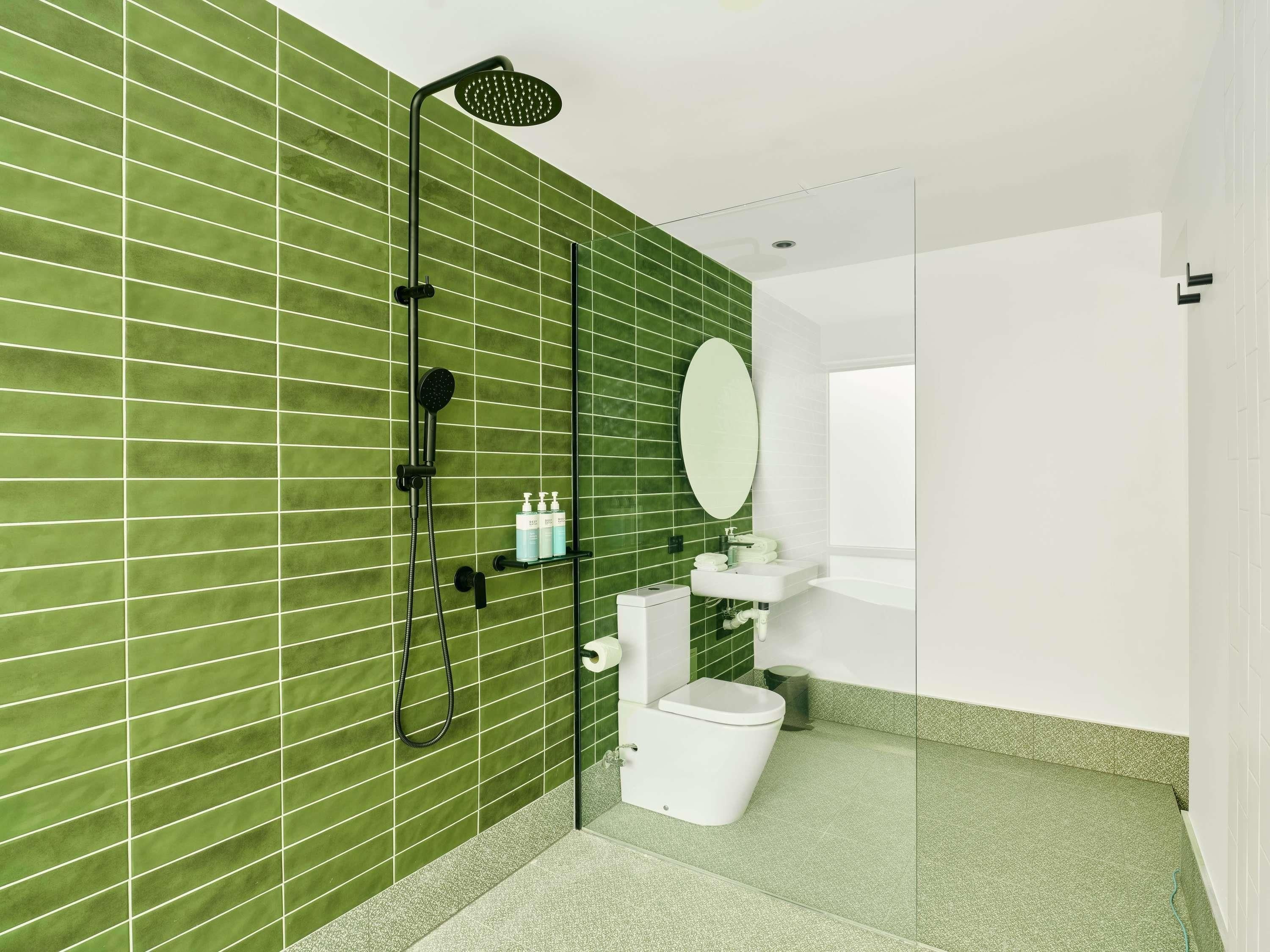 A bathroom with a green tiled wall, a shower, a toilet, a sink, and a mirror.