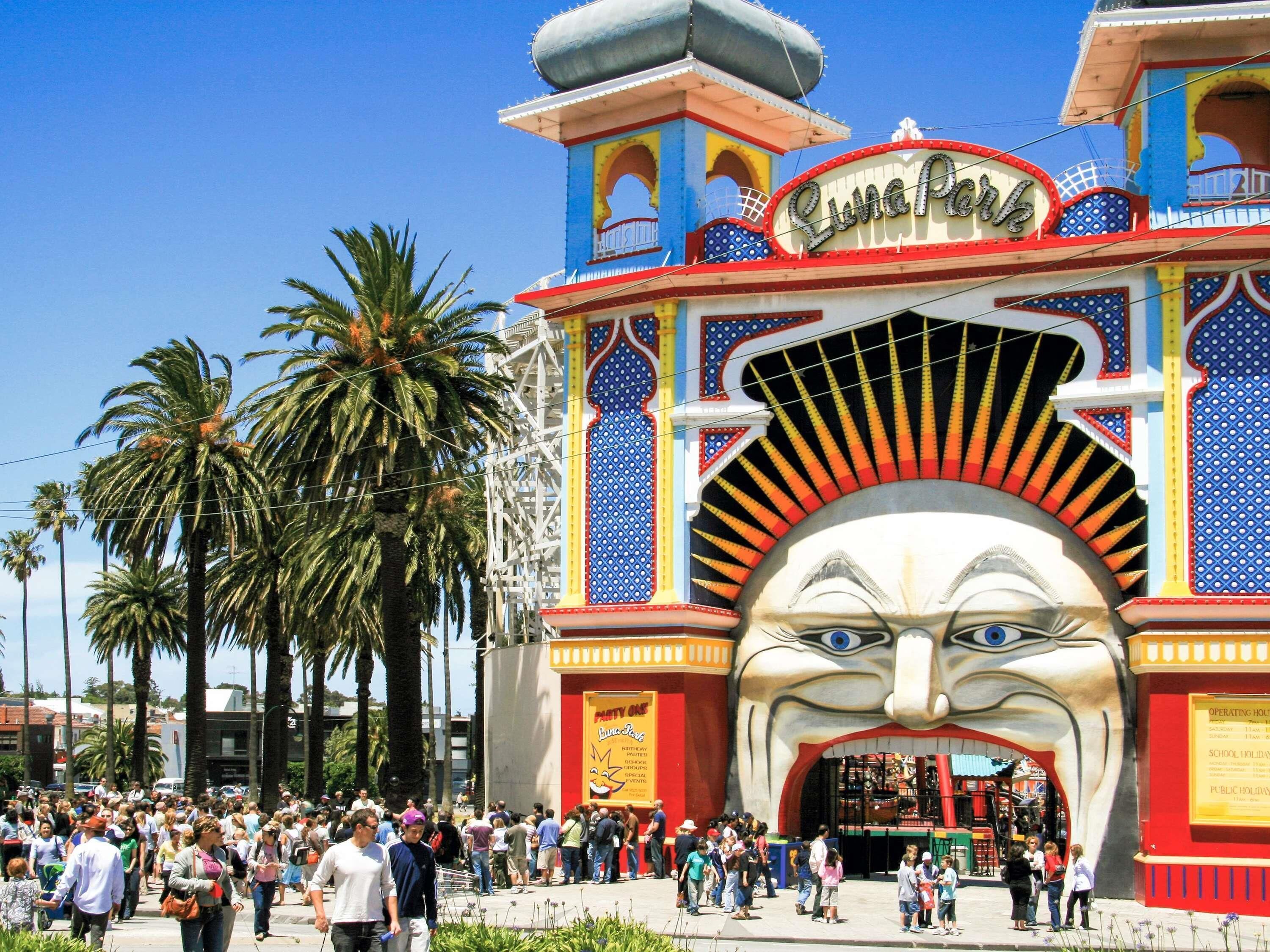 A colorful entrance with a large mural, palm trees, and a crowd of people.