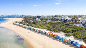 A beach with colorful beach huts and a city skyline in the background. - Novotel St Kilda (St Kilda)