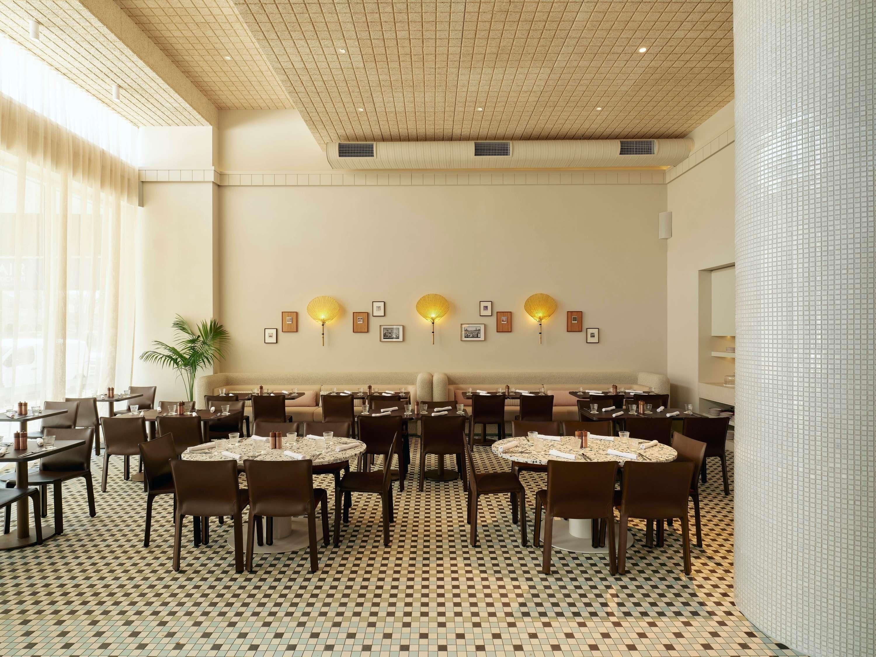 Un comedor de hotel con mesas redondas, sillas y lámparas decorativas en la pared.