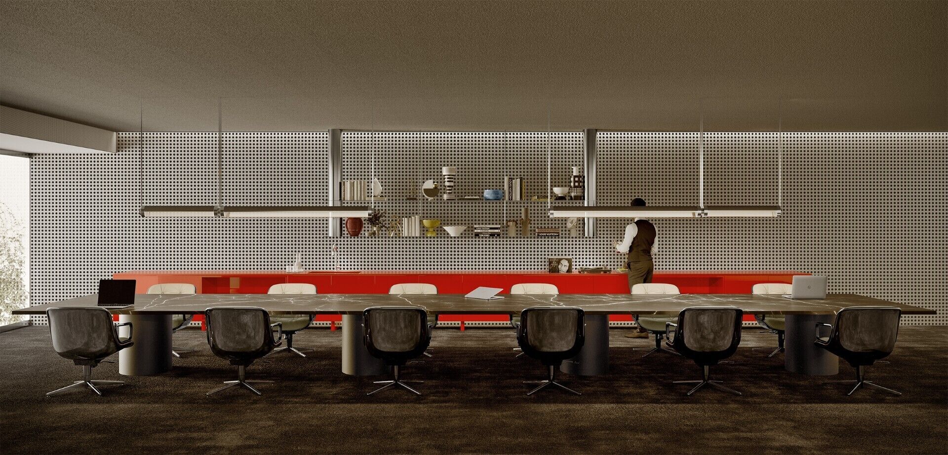 Une salle de conférence avec une longue table, de nombreuses chaises, une personne debout près du fond de la pièce et un mur perforé à l’arrière.