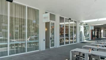 A modern outdoor seating area with tables and chairs, large windows, and a sign indicating a restaurant.