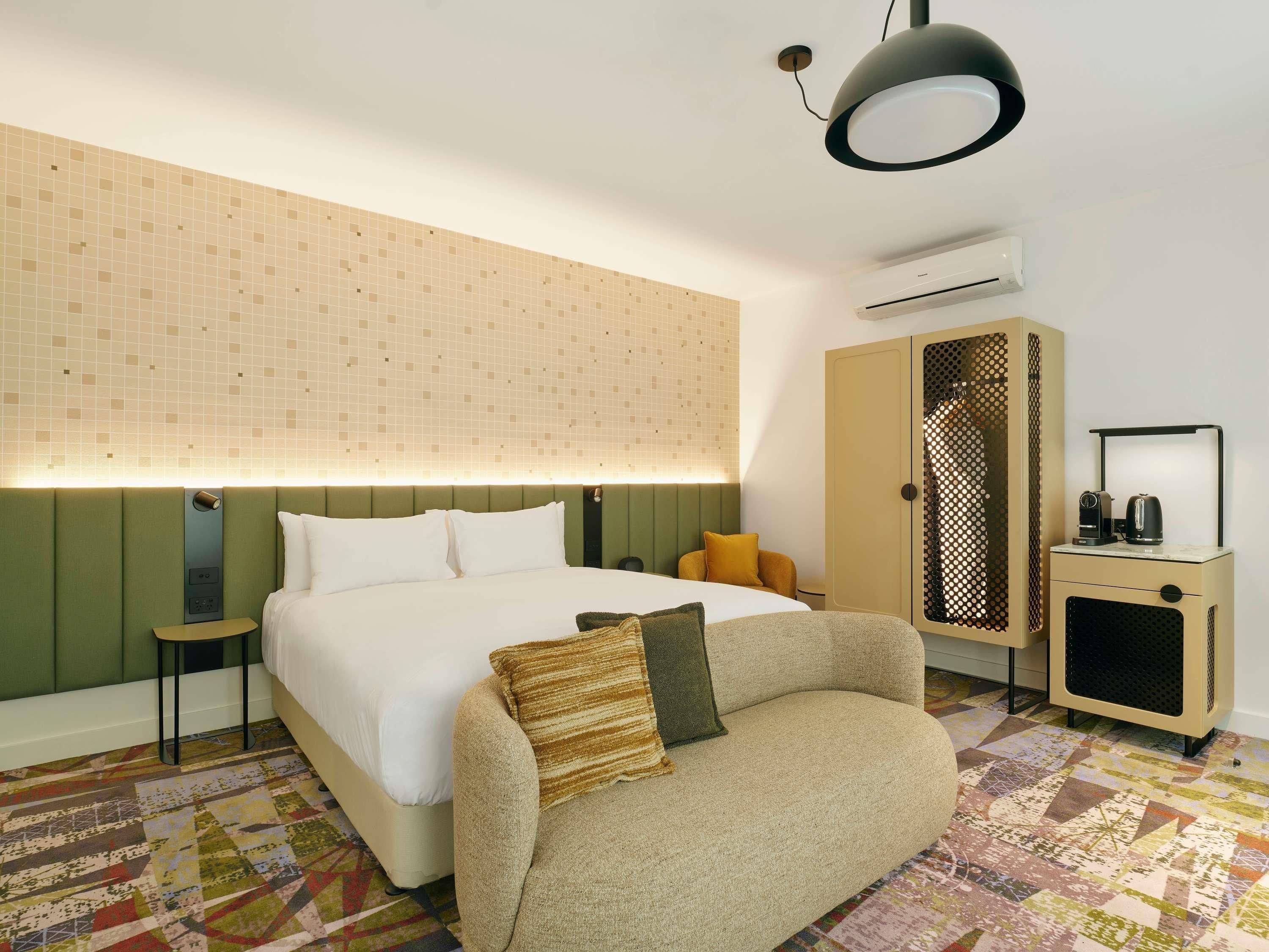 Quarto de hotel com cama, sofá, armário e pequena mesa com chaleira.