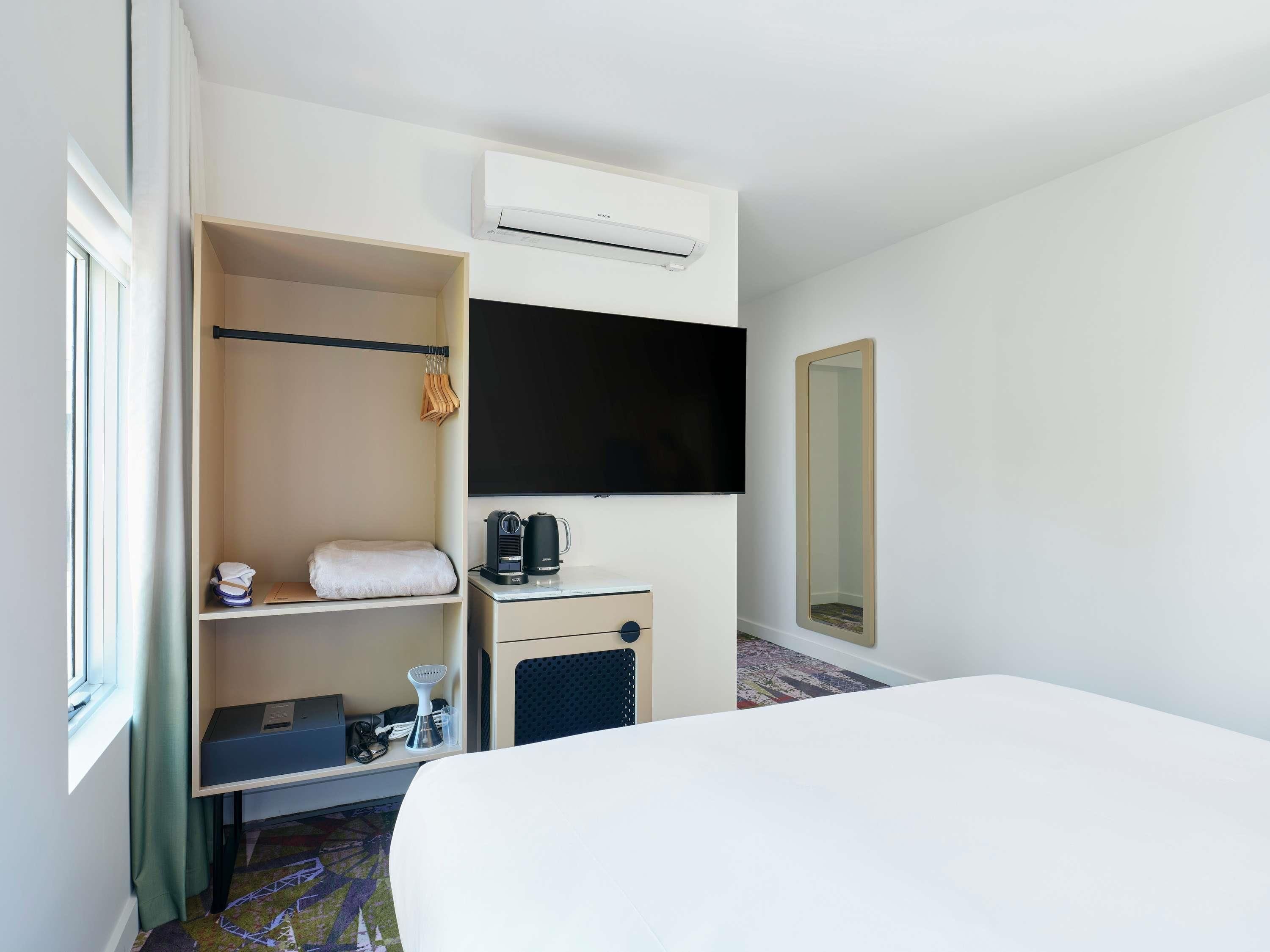 A hotel room with a bed, a wardrobe, a flat-screen TV, a coffee maker, and a mirror.