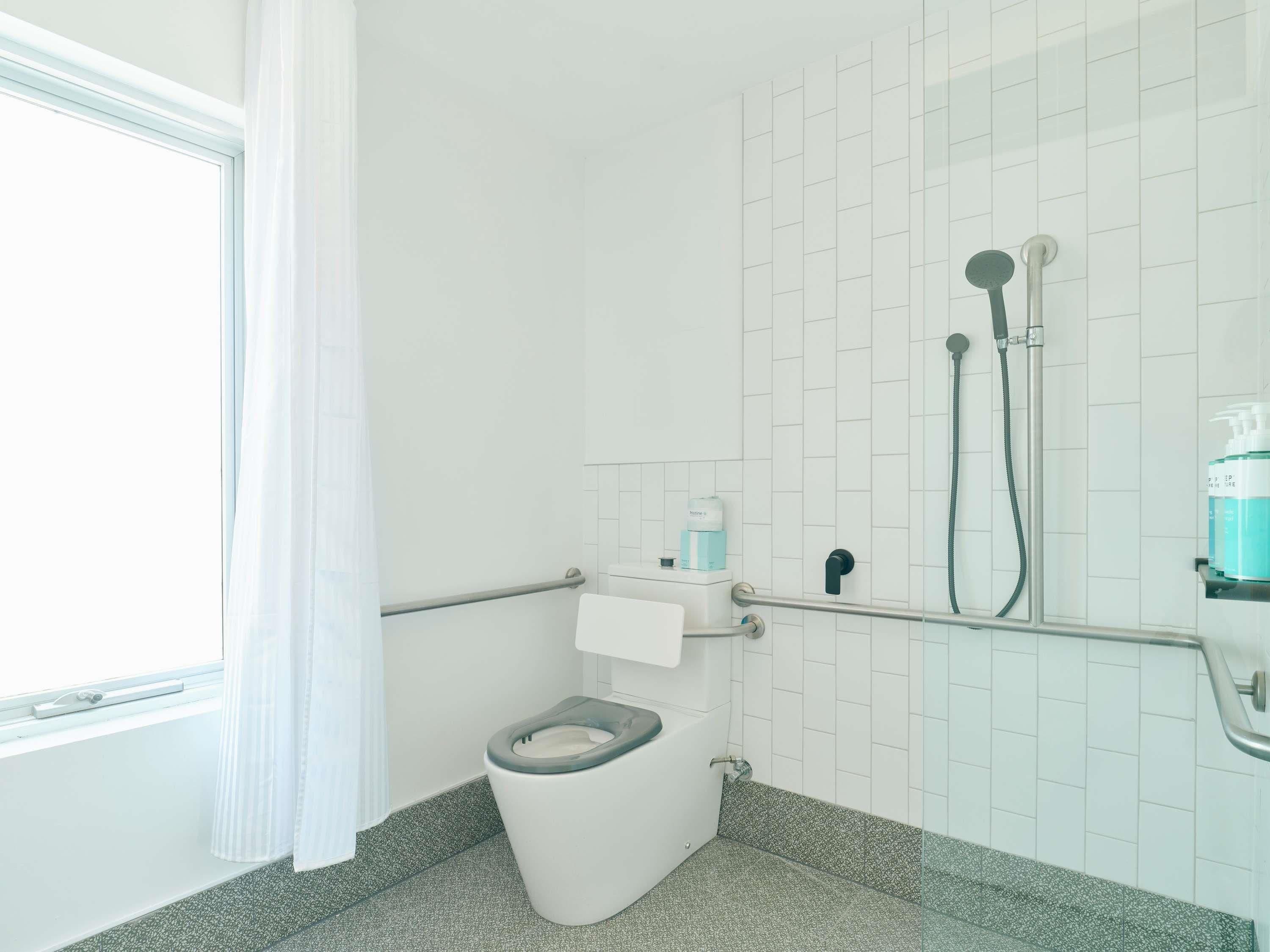 A modern bathroom with a toilet, shower, and handrails.