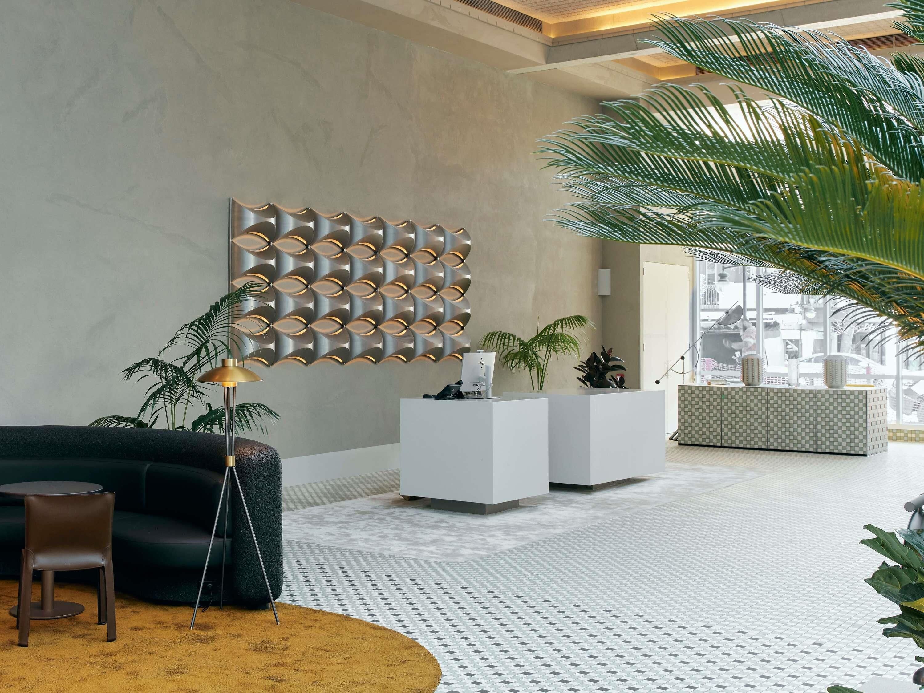 Un hall d’entrée moderne avec un comptoir d’accueil, un canapé sombre, une lampe sur pied et une grande plante en pot.