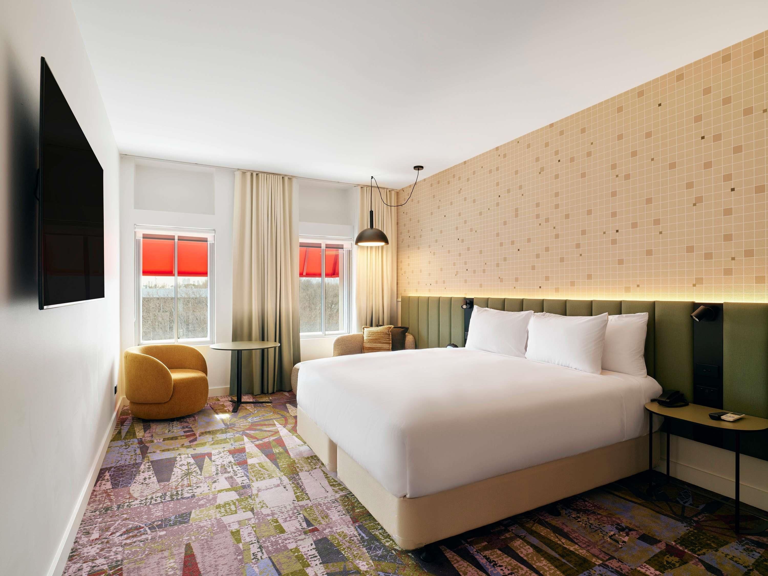 A hotel room with a large bed, a desk, a chair, and a TV.