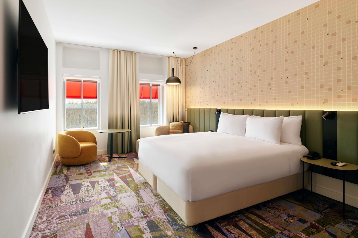 A hotel room with a large bed, a desk, a chair, and a TV.