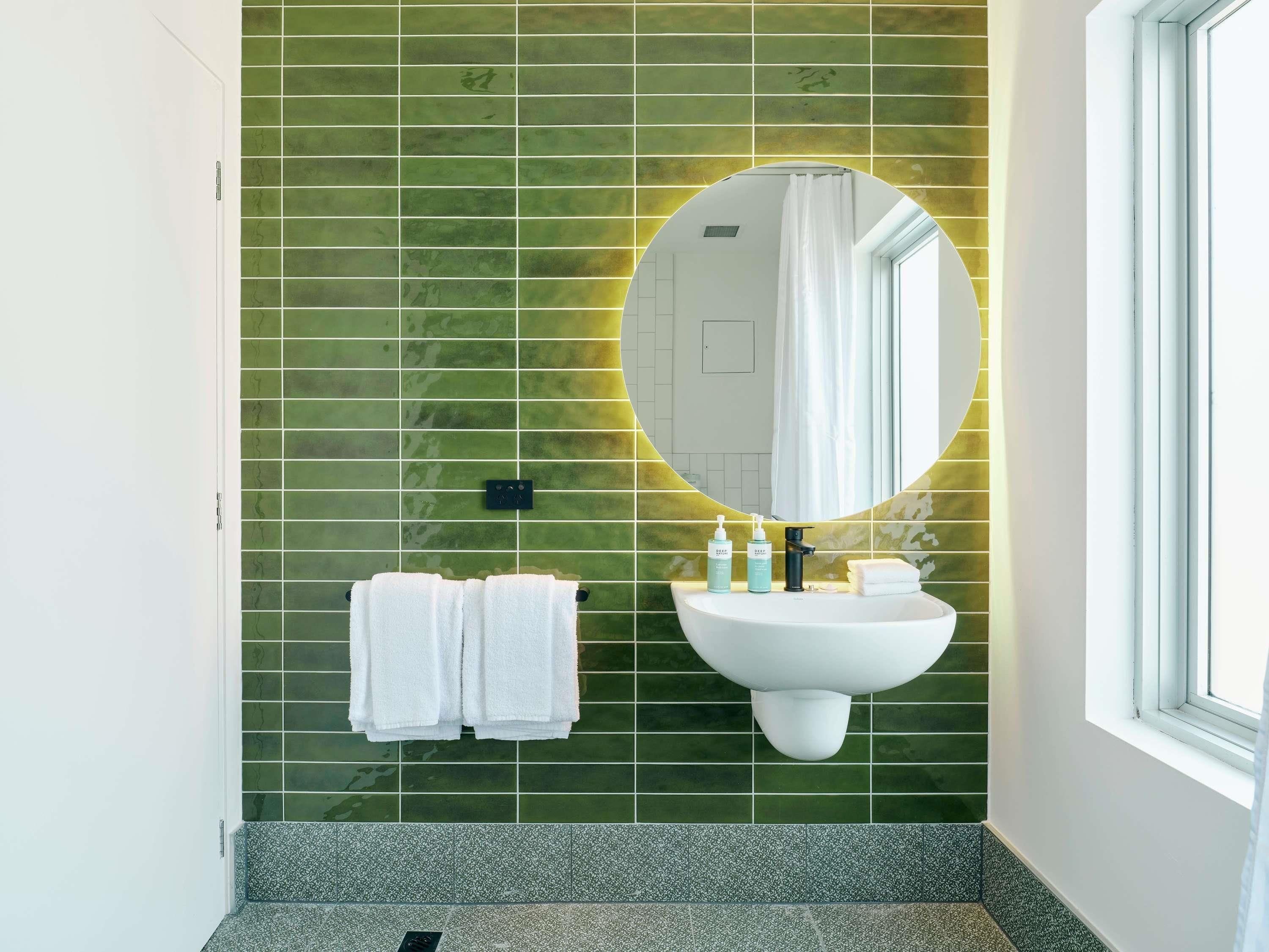 A bathroom with a green tiled wall, a white sink, a mirror, and a window.
