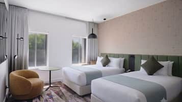 Une chambre d’hôtel avec deux lits, une chaise, une petite table et une fenêtre avec des rideaux.