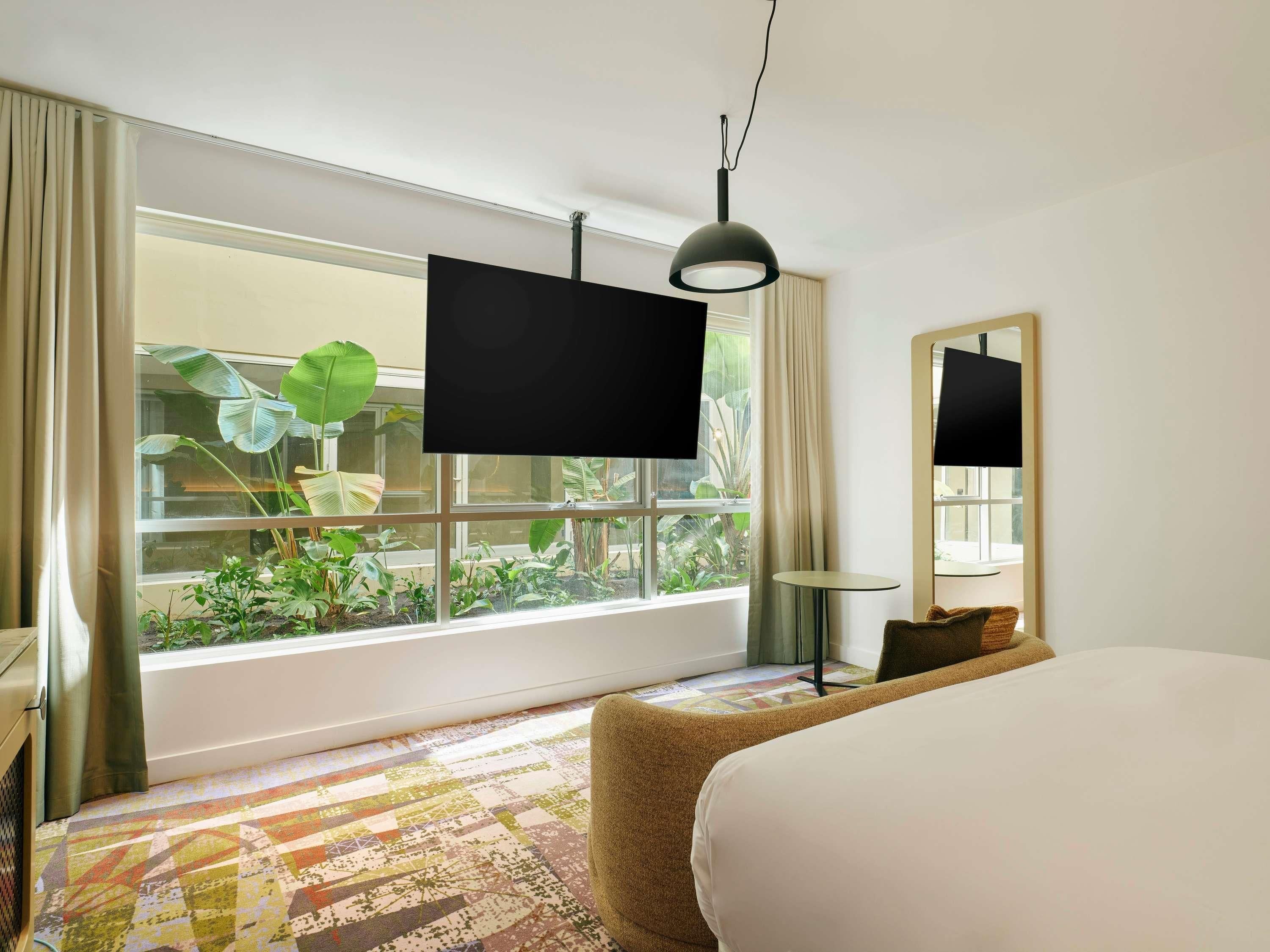 Habitación de hotel con un ventanal grande, una cama, una mesita y un espejo.