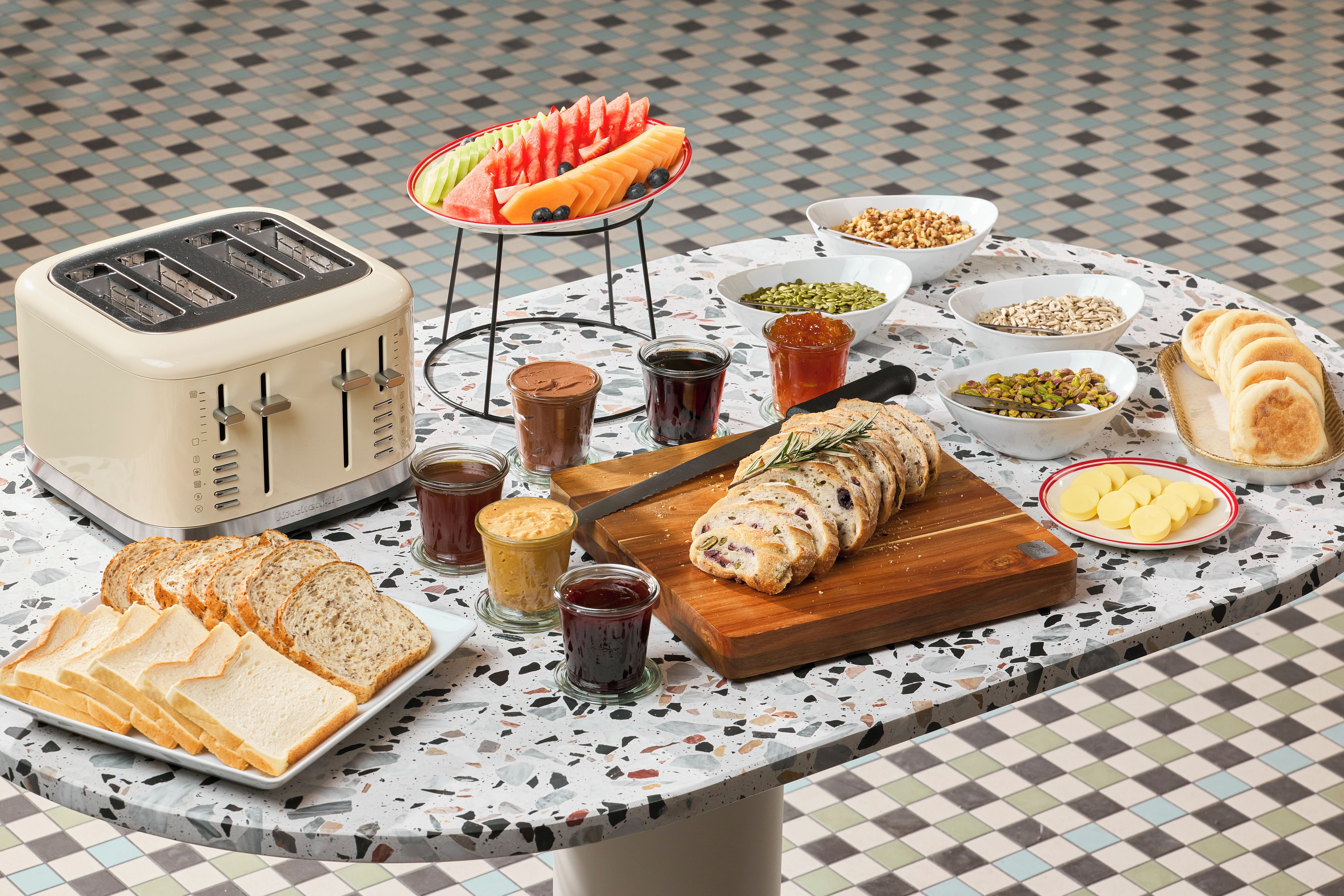 A breakfast table with various food items, a toaster, and a knife on a speckled countertop.