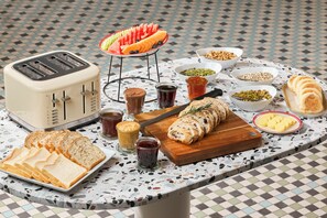 A breakfast table with various food items, a toaster, and a knife on a speckled countertop. - Novotel St Kilda (St Kilda)
