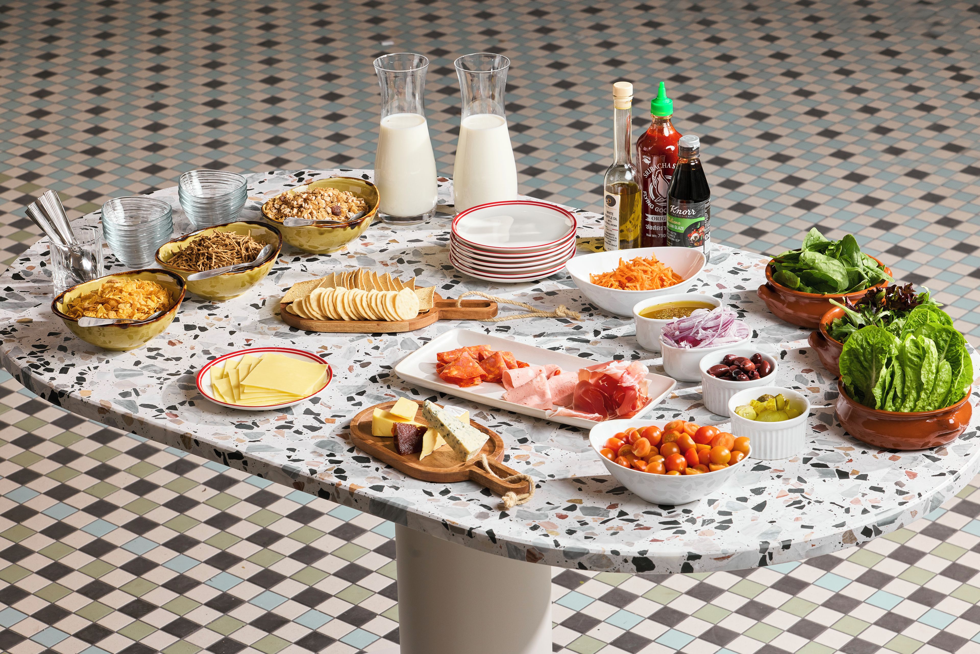 A table with various food items and condiments, including cheese, meats, and vegetables.