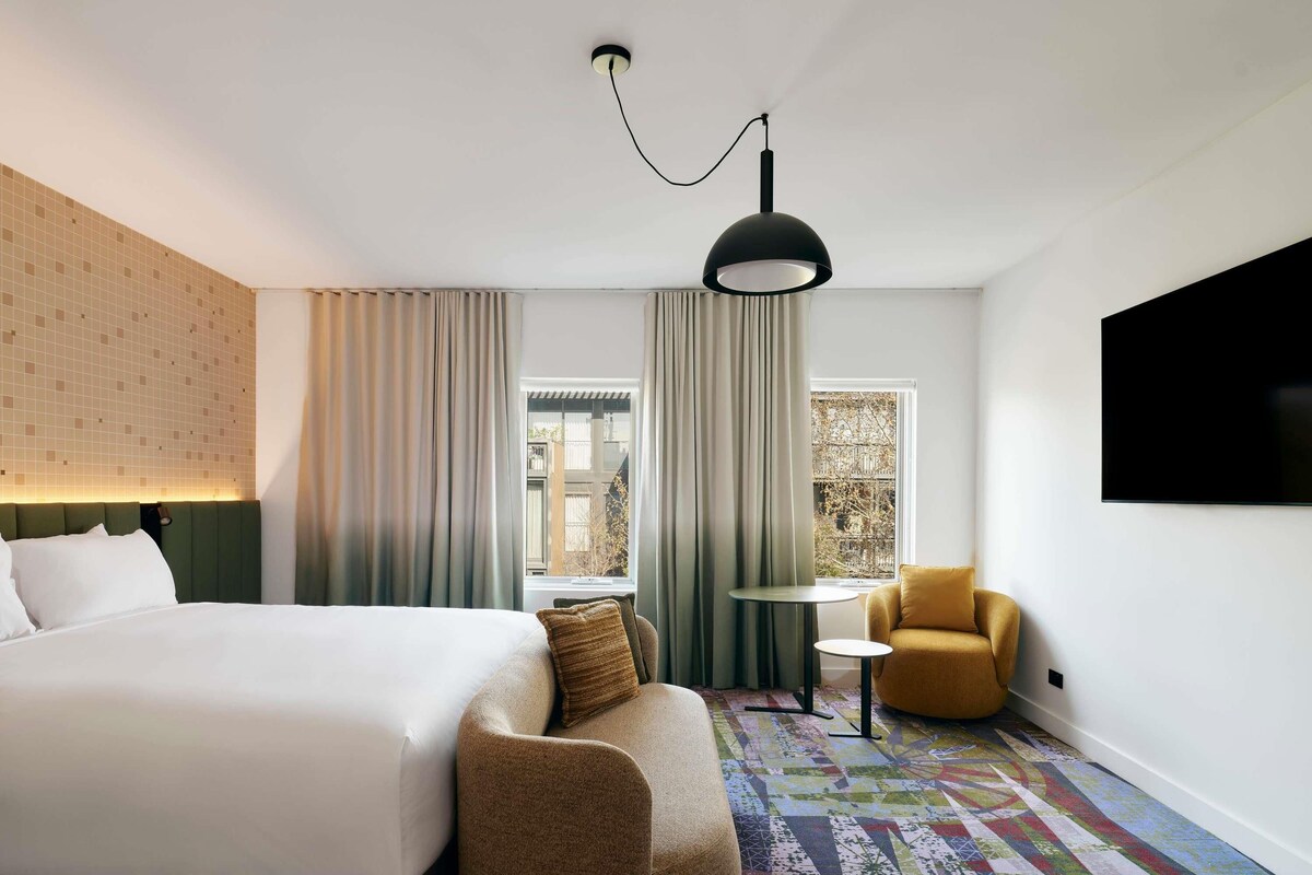 A hotel room with a bed, a sofa, a small table, a TV, and a window with curtains.