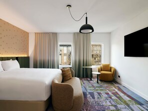 A hotel room with a bed, a sofa, a small table, a TV, and a window with curtains. - Novotel St Kilda (St Kilda)