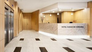 Zona de recepción de un hotel con mostrador de mármol, paneles de madera y un ascensor.
