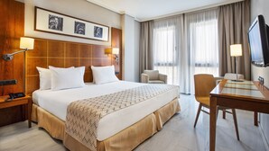 Habitación de hotel con una cama grande, un escritorio, una silla, un televisor y un teléfono en la mesita de noche.