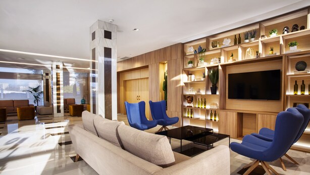 Una sala de estar moderna con un sofá, dos sillones azules, una mesita de centro y un televisor montado en una pared de madera.