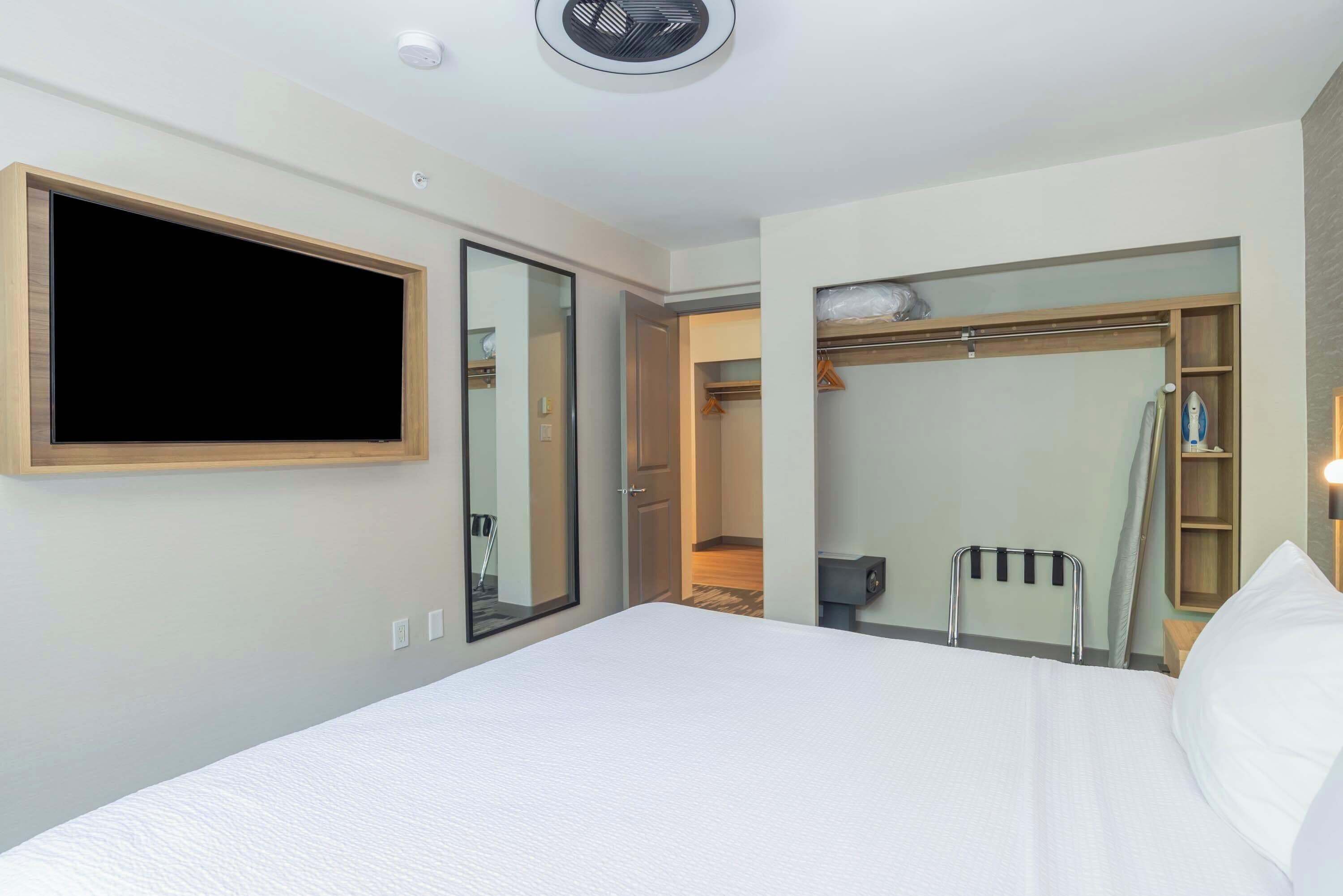 A hotel room with a large bed, a TV mounted on the wall, a walk-in closet, and a small ironing board.