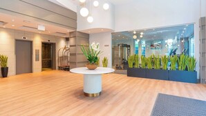 A modern lobby with a round table, potted plants, and a glass wall. - Sandman Signature Surrey-Guildford Suites (Surrey)