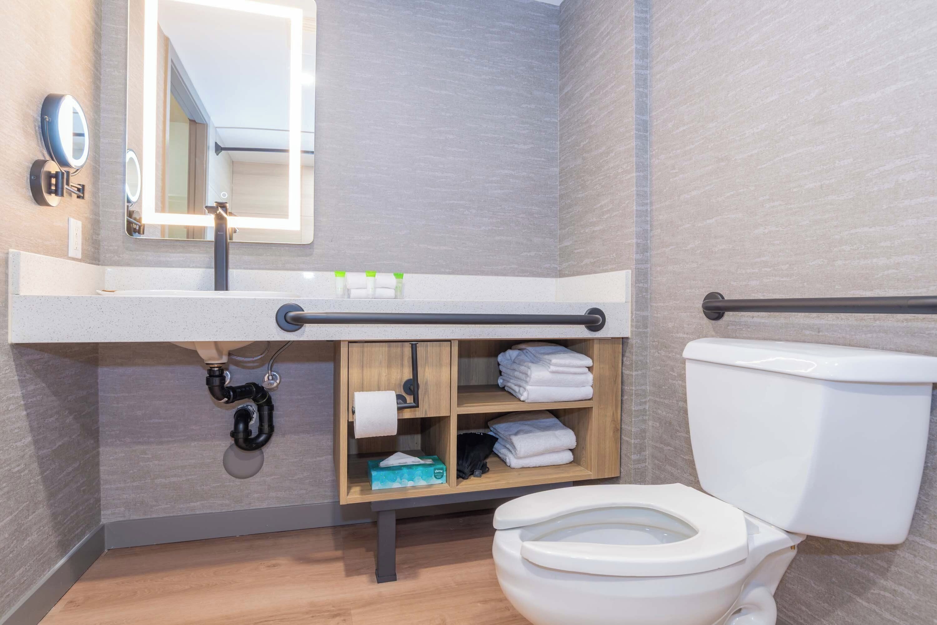 A modern bathroom with a toilet, a sink with a mirror, and a shelf with towels and toiletries.