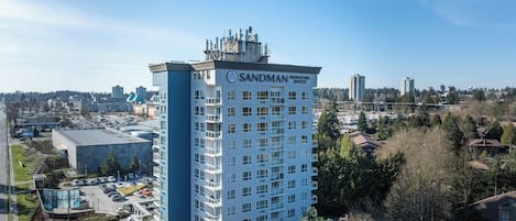 Un hotel de gran altura con varios pisos, un letrero llamativo de Sandman Signature Suites y un área de estacionamiento al frente.