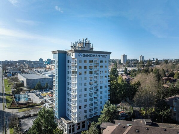 Un hotel de gran altura con varios pisos, un letrero llamativo de Sandman Signature Suites y un área de estacionamiento al frente.
