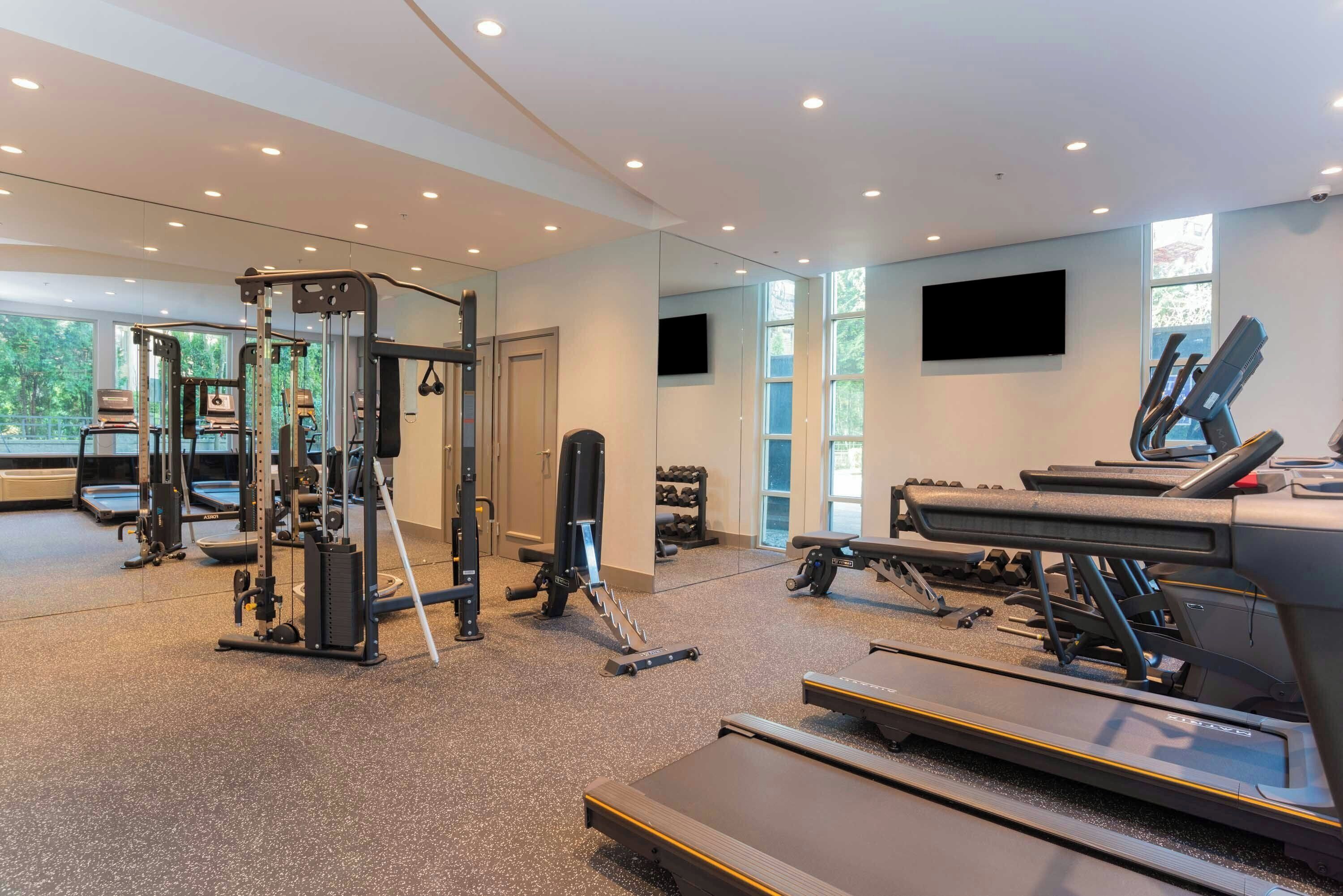 A gym with treadmills, weight machines, and a mirror wall.