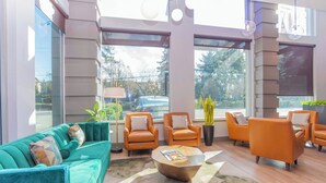 A modern lobby with a teal sofa, orange armchairs, a coffee table, and large windows offering a view of the street. - Sandman Signature Surrey-Guildford Suites (Surrey)