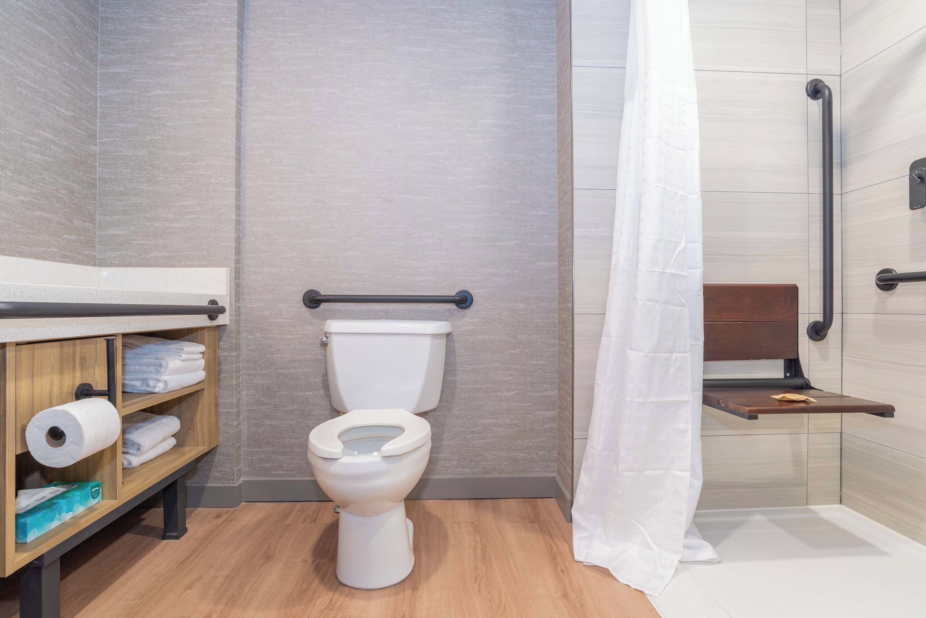 A modern bathroom with a toilet, a wooden shelf with towels, and a shower area.